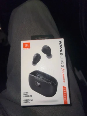 JBL Wave Buds 2 trådlösa hörlurar - Snygga svarta trådlösa in-ear hörlurar från JBL, modell Wave Buds 2. Kommer med ett kompakt laddningsetui och har aktiv brusreducering samt lång batteritid. Perfekta för musik, samtal och gaming. Modern design och smidig passform.