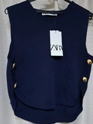 Mörkblå ärmlös topp från Zara - Snygg mörkblå ärmlös topp från Zara med guldfärgade knappar på sidorna. Toppen har en rund halsringning och en stilren, något lös passform. Perfekt att styla med jeans eller kjol för en trendig look.
