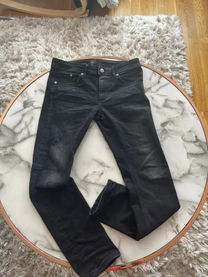 Svarta jeans från River Island -  Köpta i England,Snygga svarta jeans från River Island med klassisk femficksdesign och raka ben. Jeansen har silverfärgade knappar och nitar samt diskreta slitningar för en cool look. Perfekta till vardagsstilen och lätta att matcha med olika outfits.