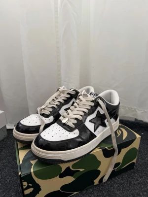 Svarta och vita BAPE STA sneakers - Säljer ett par klassiska BAPE STA sneakers i svart och vitt med den ikoniska stjärnan på sidan. Skorna har vita snören, perforerad tåbox och svartvit yttersula. Ovandelen är i glansigt läder och insidan är vit med BAPE-logga på plösen. Pris kan diskuteras!!!!!