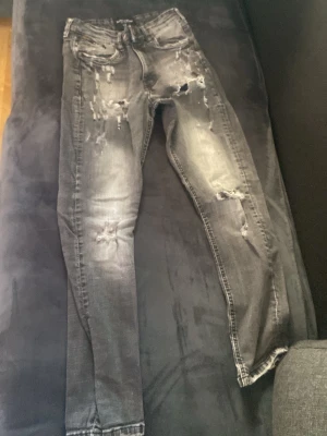 Grå slitna skinny jeans - Säljer ett par grå skinny jeans med slitningar och hål på både fram- och baksida. Jeansen har en tvättad look och klassisk femficksmodell. Perfekta för dig som gillar en edgy och trendig stil.