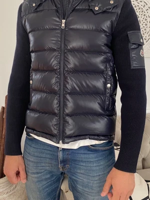 Moncler Maglione Tricot Cardigan Navy Blue - Elegant och mångsidig Moncler cardigan i den stilrena kulören navy blue. Perfekt som vår och höstjacka, men fungerar minst lika bra under mildare vinterdagar tack vare sin lätta men värmande konstruktion.  En modell som verkligen sticker ut på ett diskret och exklusivt sätt, som dessutom inte längre finns i sortimentet, vilket gör detta till ett unikt tillfälle att förvärva något som inte alla andra har.  Jackan är sparsamt använd vid ett fåtal tillfällen och är i mycket fint skick. Inga skador 