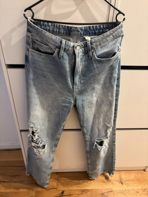 Ljusa loose fit jeans med hål - Säljer ett par ljusblå loose fit jeans från &Denim med raka ben och hög midja. Jeansen har slitna detaljer och stora hål på båda knäna för en trendig, avslappnad look. Perfekta för dig som gillar streetstyle och bekväma outfits.