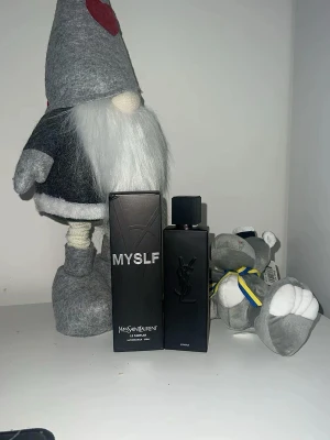 Yves Saint Laurent MYSLF Eau de Parfum - Säljer en elegant parfym från Yves Saint Laurent, MYSLF Eau de Parfum. Flaskan är svart och rektangulär med YSL-loggan i relief på framsidan. Förpackningen är också svart med vit text. Innehåller 100 ml och har en modern, stilren design.