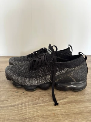 Nike air vapormax flyknit-svart/grå-Bra skick - Säljer ett par snygga och bekväma Nike Air VaporMax Flyknit i svart/grå färg. Skorna är använda men fortfarande i bra skick och fungerar som de ska. Perfekta både till vardag och träning.  ✅ Original Nike VaporMax ✅ Bekväm och lätt Flyknit-design ✅ Luftsula med bra dämpning ✅ Stilren färg som passar till allt  Skick: Använda med normalt slitage. Kartong: Finns tyvärr inte kvar.  Kan skickas eller mötas upp. Hör av dig vid frågor eller fler bilder!