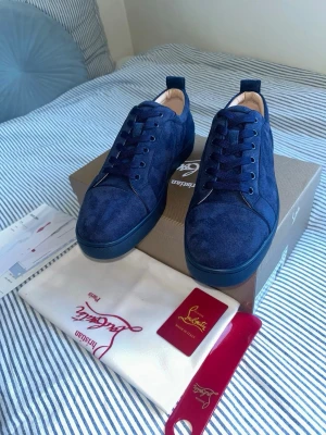Blå mockasneakers från Christian Louboutin - Snygga sneakers i djupblå mocka från Christian Louboutin. Skorna har klassisk låg profil, rund tå och matchande blå snörning. Yttersulan är också blå och insidan är ljusbeige. Perfekta för dig som vill sticka ut med exklusiva detaljer.