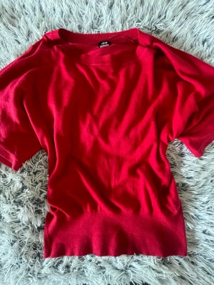 Röd kortärmad topp från H&M - Används en gång. Snygg röd topp från H&M med korta ärmar och rund halsringning. Tillverkad i mjukt material som känns skönt mot huden. Perfekt att styla med jeans eller kjol för en trendig look.