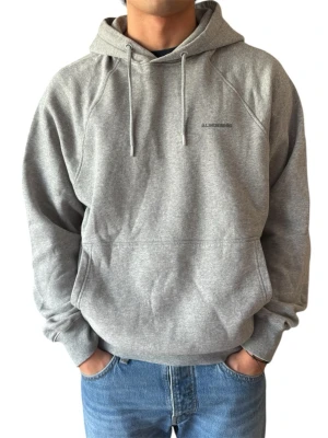 Grå hoodie från J.Lindeberg - Snygg grå hoodie från J.Lindeberg med diskret logga på bröstet. Klassisk modell med huva och dragsnören samt en stor magficka. Tillverkad i mjuk bomullsblandning och har ribbade muddar vid ärmslut och midja. Perfekt för en avslappnad stil. Modell är 182 cm
