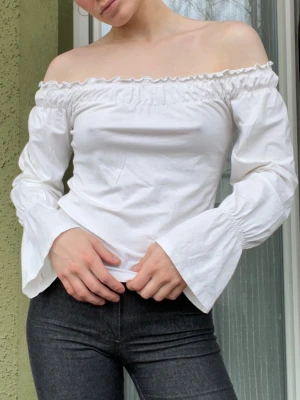 Vit offshoulder blus med vida ärmar - Superfin vit offshoulder blus med långa, vida ärmar och smockad kant upptill. Perfekt för dig som gillar romantisk och trendig stil. Tillverkad i mjuk bomull som känns skön mot huden.