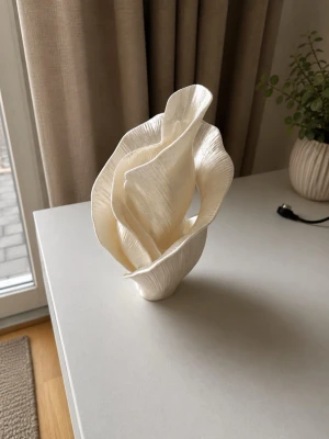 Vit dekorativ skulptur i modern design - Säljer en unik, vit dekorationsskulptur med organiska, böljande former. Skulpturen är tillverkad i ett lätt material och har en matt, strukturerad yta som påminner om blad eller vågor. Perfekt som inredningsdetalj för att ge rummet en stilren och konstnärlig touch.
