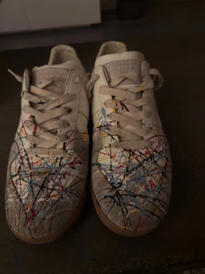 Gats med paintsplash - Tjena säljer nu dessa Maison Margiela skor. Unika Gats sneakers i vitt läder med coola färgstänk i blått, rött, svart och gult. Klassisk låg modell med gummisula och snörning. Perfekta för dig som vill sticka ut med en kreativ och konstnärlig vibe. Nypris:8000 kr. Använda fåtal gånger. Skobox medföljer självklart! PRIS GÅR ATT DISKUTERA!!