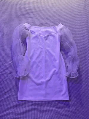 Vit klänning med puffiga armar - Trendig vit kortklänning med offshoulder och långa puffiga armar. Klänningen har en figurnära passform och är perfekt för studenten eller andra evenemanget . Skriv om du undrar något