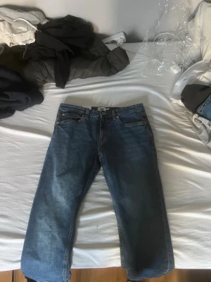 Blå raka jeans från lager 157 - Säljer ett par klassiska blå jeans från Levi's med rak passform och fem fickor. Jeansen har en tidlös denimlook och är perfekta för en avslappnad stil. Materialet är bomullsdenim och de har en 157 läderpatch bak i midjan.