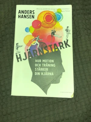 Hjärnstark av Anders Hansen - Boken 'Hjärnstark' av Anders Hansen handlar om hur motion och träning stärker din hjärna. Omslaget är vitt med färgglada illustrationer och svart text. Perfekt för dig som vill förstå sambandet mellan fysisk aktivitet och mental hälsa.