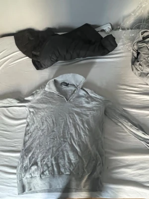 Ljusgrå tröja med krage - Säljer en stilren ljusgrå tröja med krage och v-ringning. Tröjan har långa ärmar och bred mudd vid ärmslut och nederkant. Perfekt för en avslappnad men ändå snygg look.