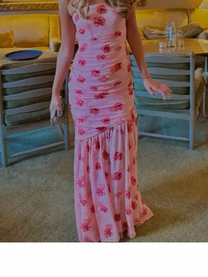 Adoore Limoges bandeau dress - Helt ny långklänning från Adoore i ljusrosa med röda blommor. Klänningen har figurnära passform upptill och volang nedtill. Perfekt för sommarens alla tillfällen! Tex midsommar eller student. 