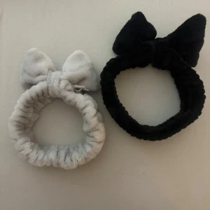 2-pack fluffiga hårband med rosett - Två mjuka och fluffiga hårband i svart och ljusgrått. Båda har en söt rosett framtill och är tillverkade i ett plyschliknande material som känns skönt mot huden. Perfekta för att hålla håret borta vid sminkning eller hudvård. Den svarta hårbandet är använt några fåtal gånger medan ljusgrå flera gånger.