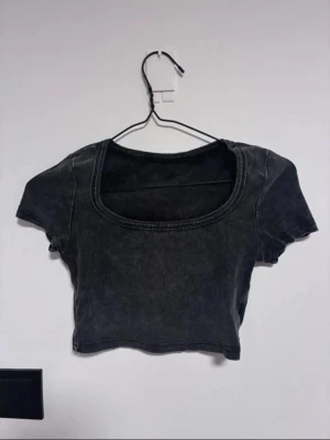Mörkgrå croppad topp från SHEIN - Snygg mörkgrå croppad topp i ribbad bomullsblandning. Endast använd en gång!  Toppen har korta ärmar och en bred, rundad urringning som ger en trendig vibe. Perfekt att matcha med höga jeans eller kjol för en cool look.