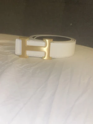 Bälte H Spänne Vändbart - Snyggt vitt skärp från H med ikoniskt H-format guldspänne. Bältet har en stilren och klassisk design som passar till många olika outfits. Tillverkat i slätt skinn med fina sömmar längs kanterna. Perfekt accessoar för att lyfta din look. Pris kan diskuteras. MVH stentorparchive⚓️