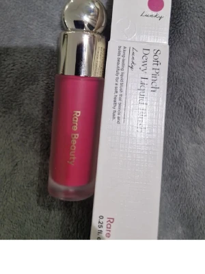 Rare Beauty Soft Pinch Dewy Liquid Blush - Rare Beauty Soft Pinch Dewy Liquid Blush i färgen Lucky. Flytande rouge med intensivt rosa ton, kommer i en frostad glasflaska med silvrigt lock och applikator. Ger en fräsch, daggig finish och är enkel att blanda ut på huden.