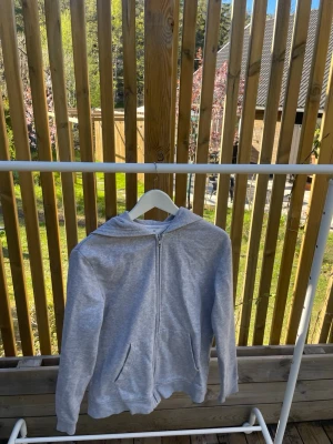 Ljusgrå hoodie med dragkedja - En stilren ljusgrå hoodie med dragkedja framtill och två fickor. Hoodien har en klassisk huva och ribbade muddar vid ärmslut och nederkant. Perfekt för en avslappnad look. Materialet känns mjukt och bekvämt. Storlek på sista bild. 