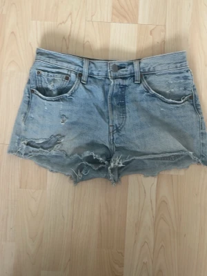 Levi's ljusblå denimshorts med slitningar - Säljer ett par ljusblå denimshorts från Levi's med rå kant och slitna detaljer. Klassisk femficksmodell med hög midja och knappgylf. Perfekta för sommaren och ger en avslappnad vintagekänsla. Ordinarie pris på 639. Pris kan diskuteras❣️