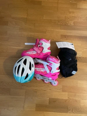 Rosa inlines med hjälm och skydd - Säljer ett set med rosa och vita inlines från Decathlon, matchande vit och turkos hjälm samt ett svart nät med skydd. Perfekt för dig som vill åka stilrent och säkert. Justerbara spännen och bekväm passform.
