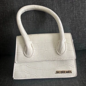Vit handväska  - Vit handväska från Jacquemus med croco-mönstrad yta och guldfärgad logga framtill. Väskan är smutsig där bak men inget man lägger märke till. 