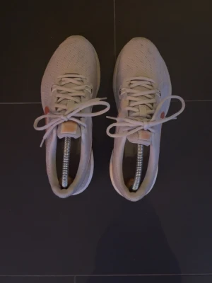 Nike grå sneakers  - Snygga grå Nike sneakers med klassisk låg profil och vit sula. Skorna har ett mönstrat meshmaterial för bra andningsförmåga och en metallic kopparfärgad swoosh på sidan. Perfekta för dig som gillar stilrena och sportiga skor.