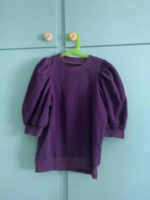 Lila topp med puffärm från Lindex - Superfin lila topp från Lindex med puffiga trekvartsärmar och rund halsringning. Mjuk och skön bomullskänsla, perfekt för dig som vill ha en trendig och bekväm look. Snygg till både jeans och kjol!