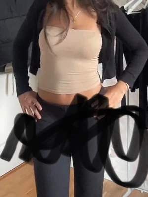Beige tubtopp i stretchigt material - Snygg beige tubtopp med bandeau-modell. Toppen är figurnära och har en enkel, stilren design utan axelband. Perfekt att matcha med jeans eller kjol för en trendig look.