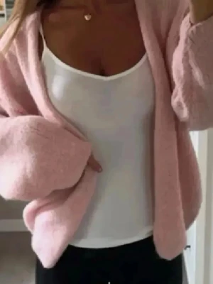 Ljusrosa fluffig stickad kofta - Supermjuk och oversized ljusrosa stickad kofta med breda ärmar och öppen front. Perfekt att slänga över en topp för en chill och trendig look. Materialet är fluffigt och ger en mysig känsla. Enkel att matcha med både jeans och leggings.