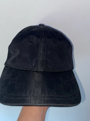 Gucci nylon keps - Snygg svart nylon keps från Gucci med diskret GG-monogram över hela kepsen. Kepsen har böjd skärm och mesh på sidorna för extra ventilation. Tillverkad i Italien och har en exklusiv känsla med klassisk design.       GÅR MED PÅ BYTEN OCKSÅ MÖTS UP I MALMÖ