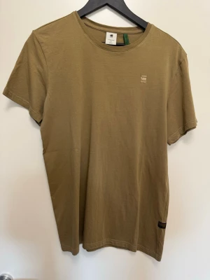 Olivgrön t-shirt från G-Star RAW - Snygg olivgrön t-shirt från G-Star RAW med rund halsringning och diskret logga på bröstet. Tillverkad i mjuk bomull för en skön känsla. Klassisk passform och korta ärmar, perfekt till jeans eller shorts.