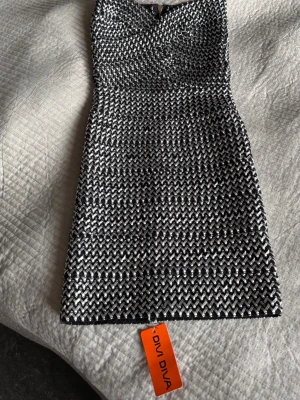 Svartvit kort klänning från Diva Diva - Snygg kort klänning från Diva Diva i svartvitt mönster med glittrig känsla. Klänningen har figurnära passform, dragkedja i ryggen och ett coolt, vävt mönster som verkligen sticker ut. Perfekt för dig som vill ha något unikt och trendigt.