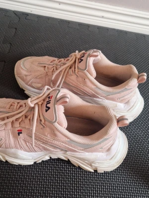 Fila chunky sneakers ljusrosa - Chunky sneakers från Fila i ljusrosa med vita och grå detaljer. Skorna har kraftig sula, snörning och Fila-logga på plösen och sidan. Tillverkade i mesh och syntetmaterial för en sportig vibe.