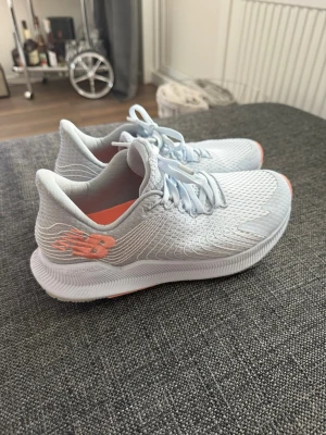  New Balance sneakers - Snygga ljusgrå/blåa sneakers från New Balance med mesh-ovandel och detaljer i ljus korall. Skorna har en sportig design, lågt skaft och bekväm sula. Perfekta för dig som gillar stilrena och fräscha sneakers med coola detaljer. Knappt använda 