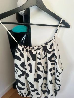 Zara svartvit one shoulder topp - Snygg linnetopp one shoulder från Zara med svartvitt zebramönster och tunt axelband. Toppen har en lös passform och resår både upptill och nertill för en cool och avslappnad look. Perfekt att styla med jeans eller kjol.