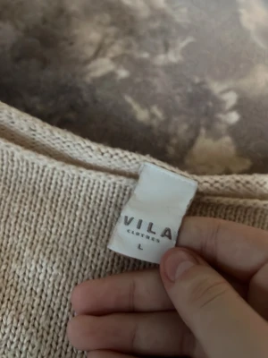 Beige stickad tröja från Vila - Snygg beige stickad tröja från Vila med rund halsringning och långa ärmar. Tröjan har en enkel och stilren design med ribbade muddar vid ärmslut och nederkant. Perfekt för lager-på-lager och passar till det mesta.