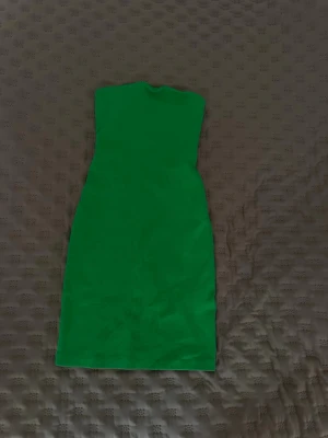 Grön axelbandslös klänning från Zara - Snygg grön axelbandslös klänning från Zara. Klänningen är kort och har en tight passform som framhäver figuren. Perfekt för dig som vill sticka ut med en färgstark look. Tillverkad i ett stretchigt material.