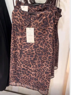Leopardmönstrad klänning från Zara - Säljer en snygg leopardmönstrad klänning från Zara med tunna axelband och figurnära passform. Klänningen har bygel vid bysten och är gjord i ett tunt, lätt material som ger en cool och trendig look. Helt ny med prislapp 