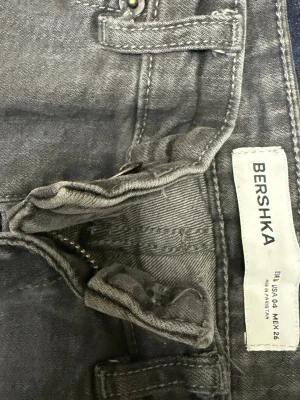 Grå jeans från Bershka bootcut - Snygga grå jeans från Bershka med bootcut-modell och klassisk femficksdesign. Jeansen har bälteshällor och dragkedjegylf. Perfekta för en trendig och avslappnad look.