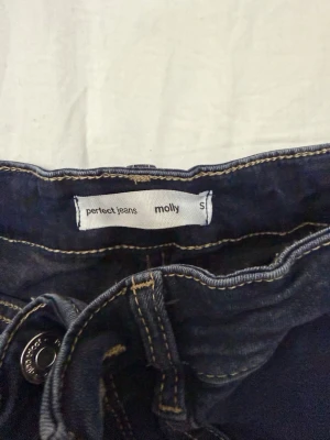 Mörkblå jeans från Perfect Jeans - Snygga mörkblå jeans från Perfect Jeans, modell Molly. Klassisk femficksdesign med kontrastsömmar och knappgylf. Jeansen har en smal passform och är tillverkade i stretchigt material för extra komfort.