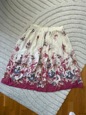 Vinted kjol i rosa och vitt - Superfin somrig kjol med blommigt mönster i rosa, vitt, blått och brunt. Kjolen har en vid och luftig passform och är perfekt för vår och sommar. Materialet känns mjukt och lätt, vilket gör den skön att bära hela dagen. Superfin vintedkjol med markerad midja. Knapp och dragkedja i sidan. Fint skick förutom några diskreta hål, se sista bild. Dem syns ej när man har kjolen på sig.