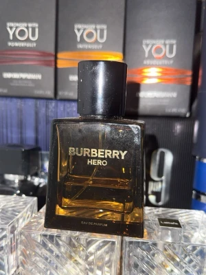 Burberry Hero Eau de Parfum 50ml - Burberry Hero Eau de Parfum i en stilren, fyrkantig glasflaska med mörk bärnstensfärg och svart kork. Flaskan rymmer 50 ml och har en lyxig känsla med tydlig Burberry-logga i guld på framsidan. Perfekt för dig som gillar exklusiva dofter. Den är 50 ml men det är kvar kanske 30 ml ingen låda borttappad köpte på kicks för 1185kr det är Herr parfym 