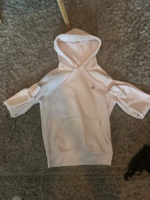 Vit hoodie från Moncler - Snygg vit hoodie från Moncler med klassisk huva och känguruficka framtill. På bröstet sitter Monclers ikoniska logotyp i vitt, svart och rött. Hoodien har en stilren design och är tillverkad i mjukt material som känns skönt mot huden. Storlek S men passar helt okej på mig som är 163 cm bara lite för stor