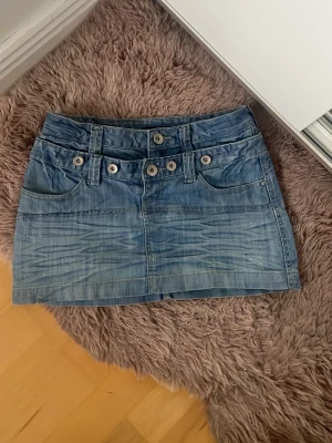 Blå jeanskjol med knappar - Snygg blå jeanskjol i kort modell med flera knappar och fickor framtill. Kjolen har en klassisk denimlook och passar perfekt till en avslappnad stil.står inte storlek men är som en xs-s. Enkel att matcha med olika toppar för en trendig outfit.hör av dig om du har frågor eller funderingar💕