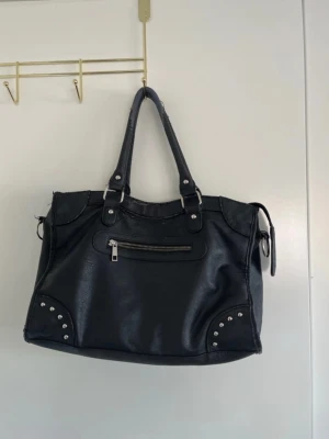 Svart väska med silver detaljer från DONDONNA - Svart väska med silver detaljer från DONDONNA. Lite slitningar vilket syns på sista bilderna. Lite torkat nagellack inuti väskan. Inget som påverkar användningen
