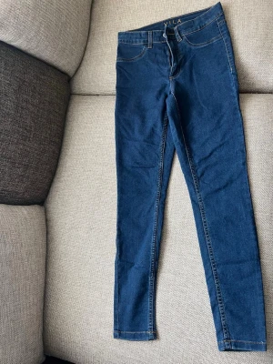 Mörkblå skinny jeans från Vila - Säljer ett par mörkblå skinny jeans från Vila med klassisk femficksdesign och guldfärgade sömmar. Jeansen har normal midja och är tillverkade i stretchigt denimtyg för en bekväm passform.