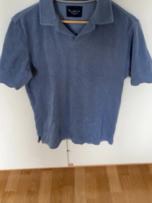 Blå frottépiké från Bondelid - Snygg blå pikétröja från Bondelid i mjuk frotté. Klassisk krage och korta ärmar ger en avslappnad look. Perfekt för dig som gillar stilrena och bekväma plagg. Enkel att matcha med jeans eller shorts.